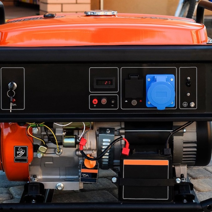 A backup electrical generator is shown. It has an orange top and some electrical components displayed on the control panel.