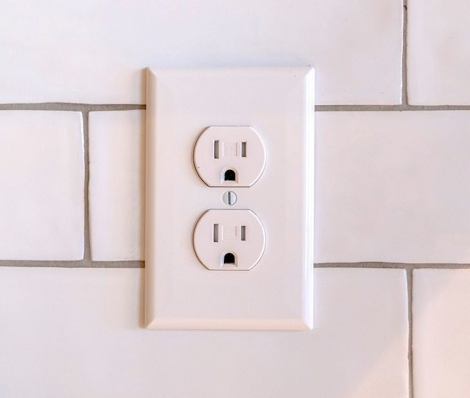 An outlet in a kitchen with white subway tile